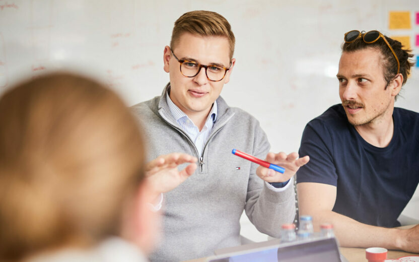 Ein Mann der seinen beiden Kollegen im Meeting eine Strategie erklärt.