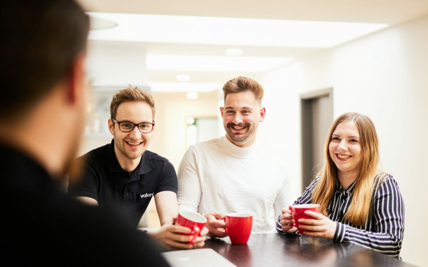 Zwei Männer und eine Frau, die zusammen an einer Office-Bar Kaffee trinken.