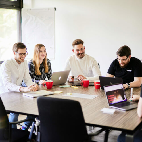 Fünf Kolleg*innen während eines Meetings in einem Konferenzraum mit Glaswänden.