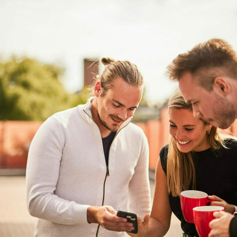 Picture of three colleagues looking at something on a smartphone during their coffee break.