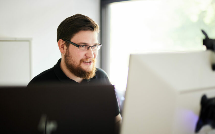 Foto von einem Mann mit Brille und Bart, der in einen Computerbildschirm schaut.