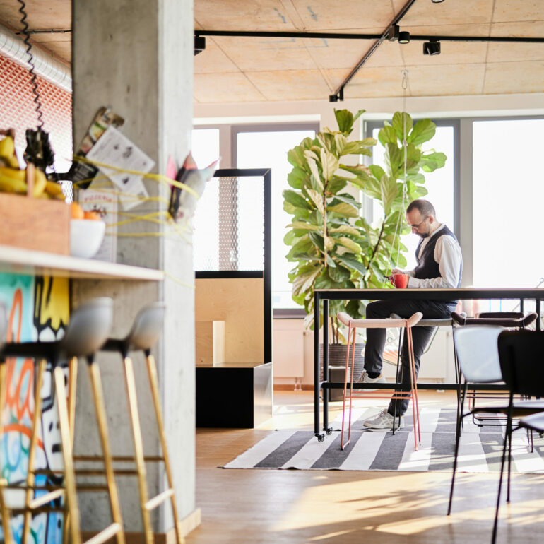 Photo of the modern break area of the valantic office Mannheim – a man sits casually on a bar stool and types on his smartphone.