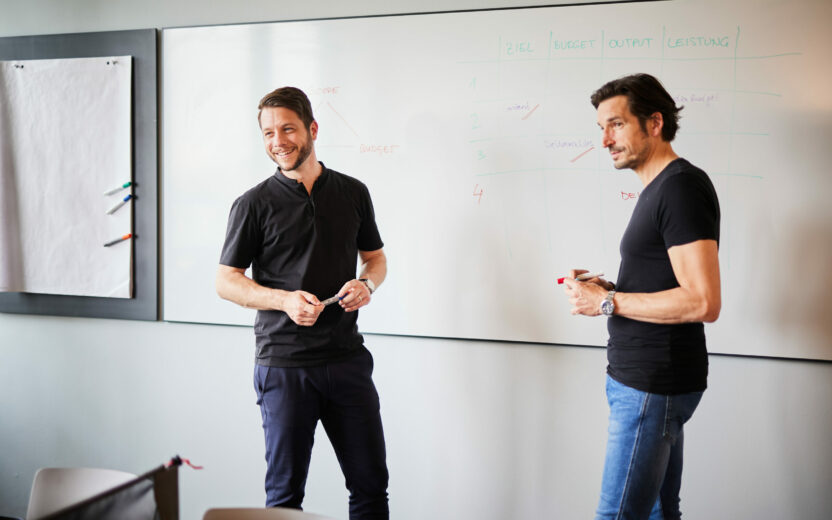 Zwei Mitarbeiter der valantic CX stehen vor einem Whiteboard und halten eine Präsentation