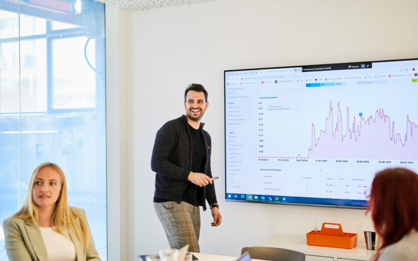 Foto von einem jungen Mann, der in einem Meeting die letzten Customer-Journey-Daten via PowerPoint vorstellt.