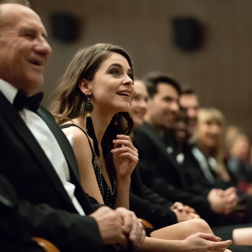 Side view of multi ethnic audience sitting in the opera. Men and women are watching theatrical performance. They are in elegant wear.