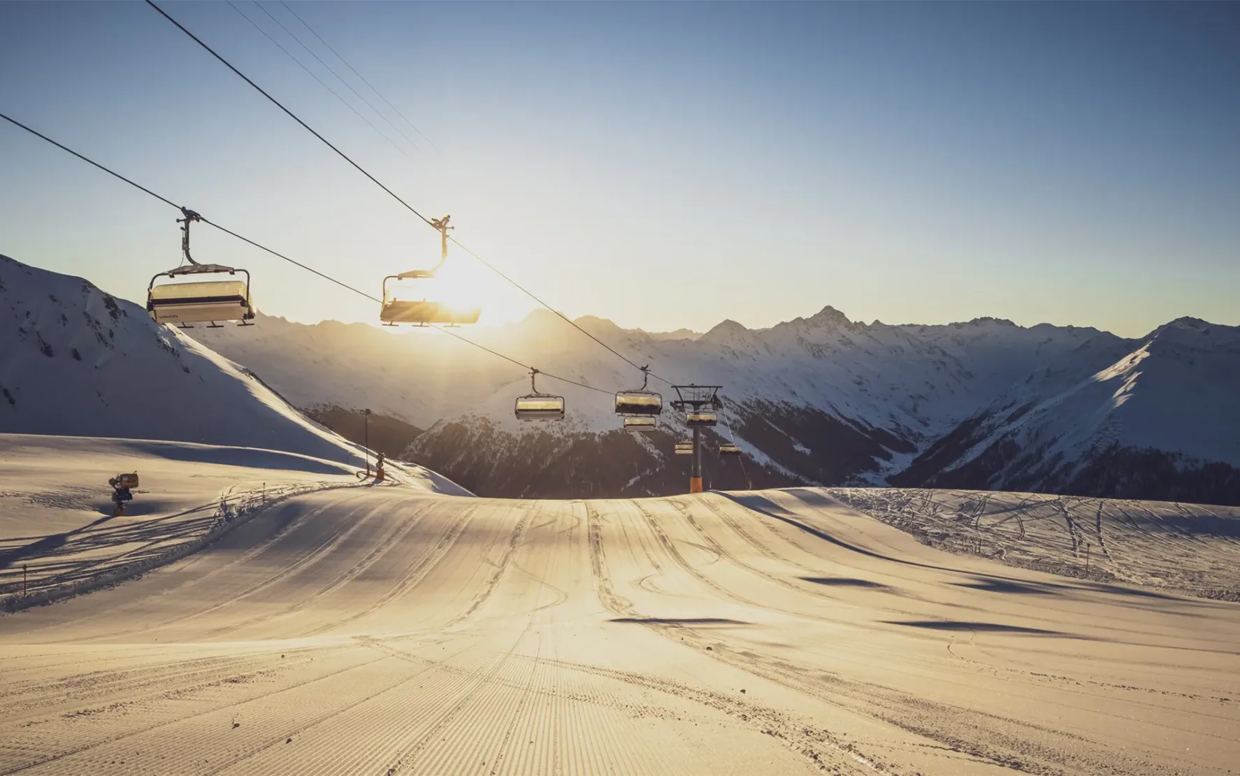 Davos Klosters Mountains Header: Zu sehen ist ein Sessellift, der im Gegenlicht über einer frisch präparierten Piste fährt.