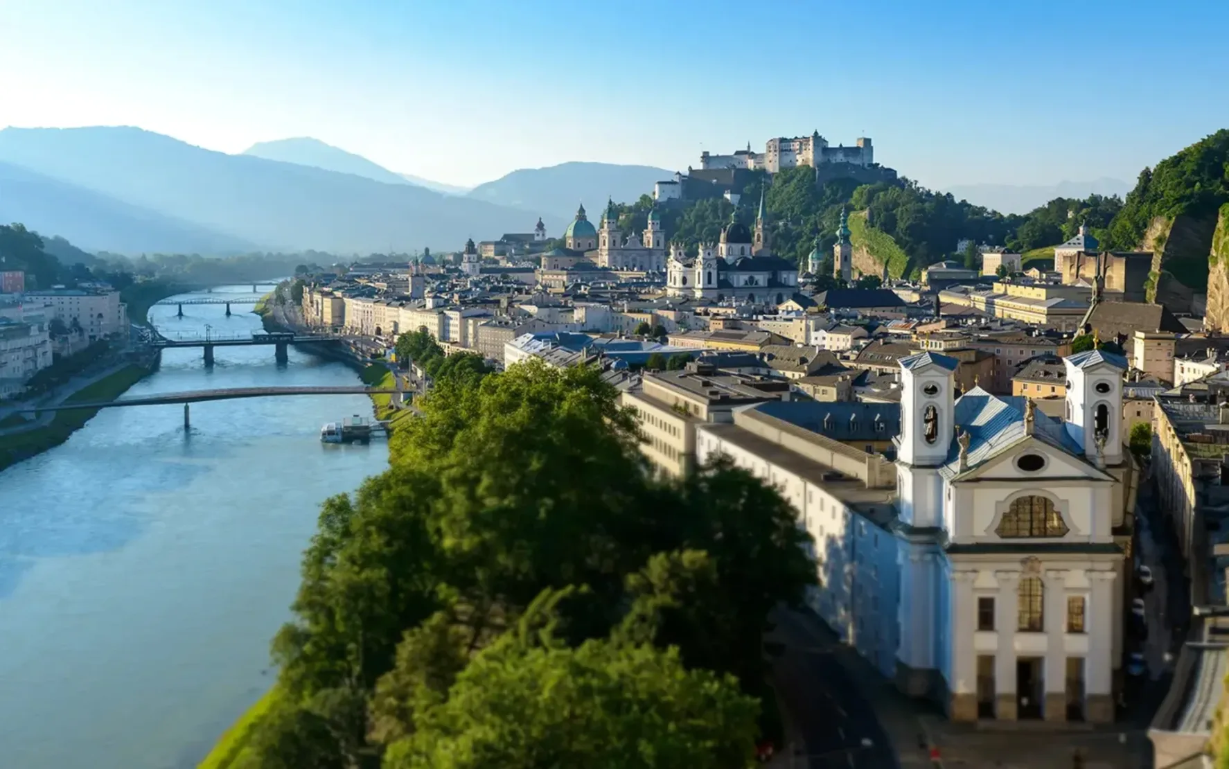 Foto von der Stadt Salzburg von oben. Zu sehen ist die Salzach, der Mönchberg mit Festung, der Salzburger Dom und die Altstadt.