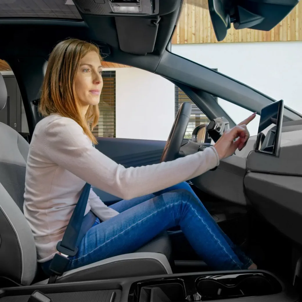 Side view of woman smiling and sitting while touching device screen in modern car.